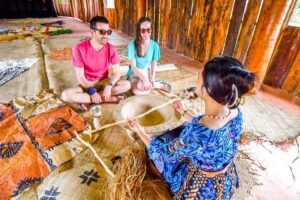 Tongan woman sitting infront of two people with Tongan handicrafts